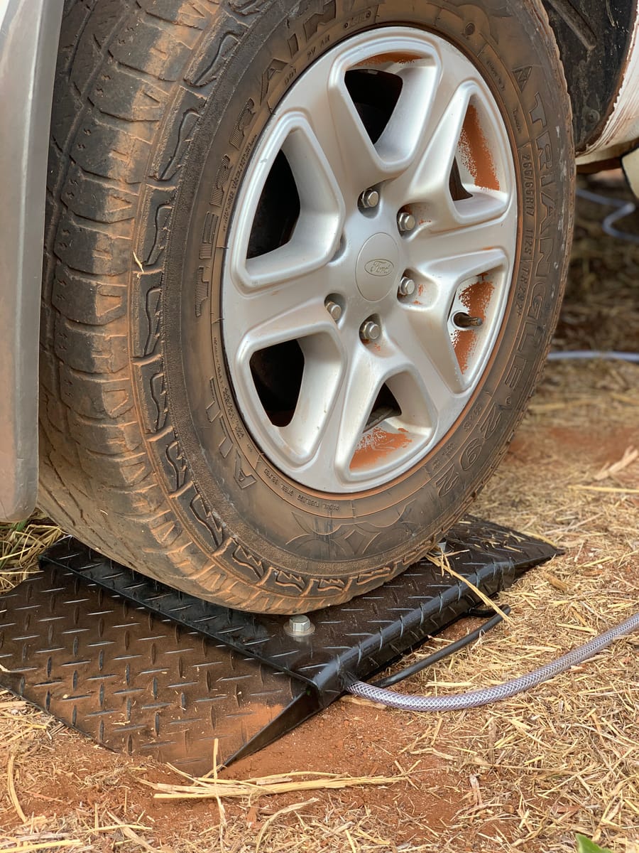 Pneu de um veículo apoiado sobre a plataforma da balança de sapata móvel Uber, em piso de terra no campo